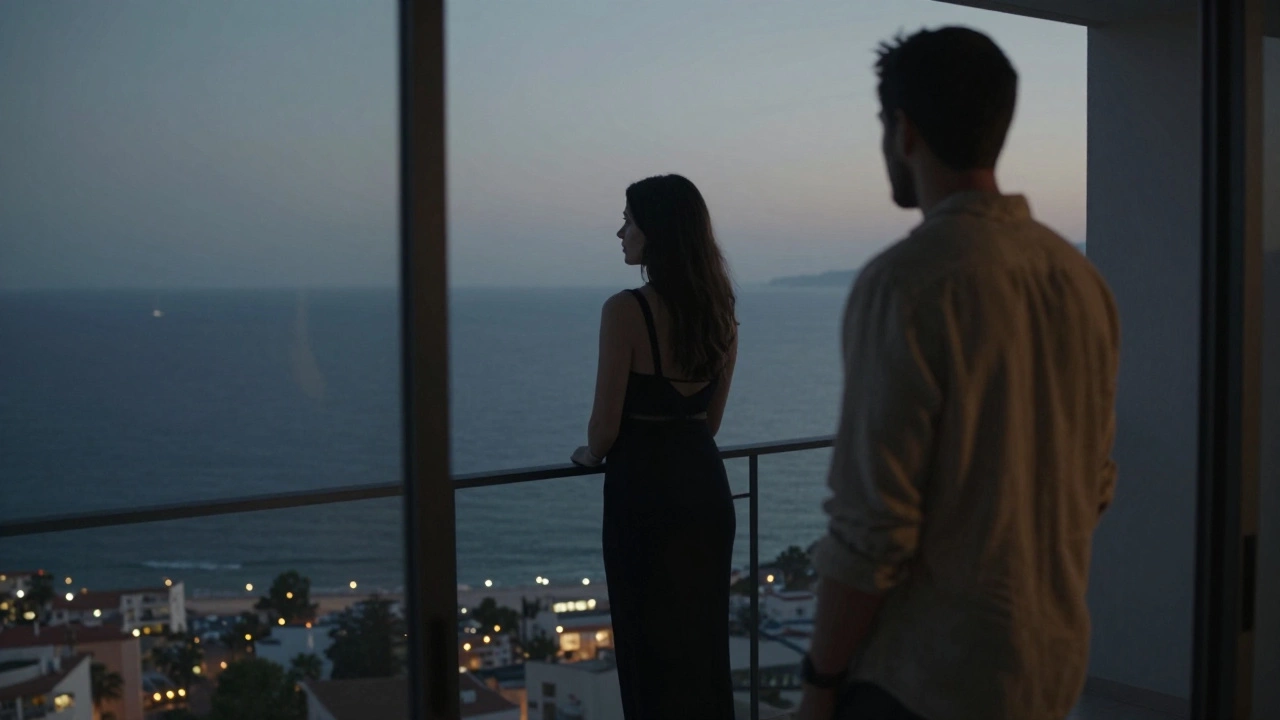 A woman stands on a balcony at twilight, overlooking Cannes, her companion watching softly from behind.